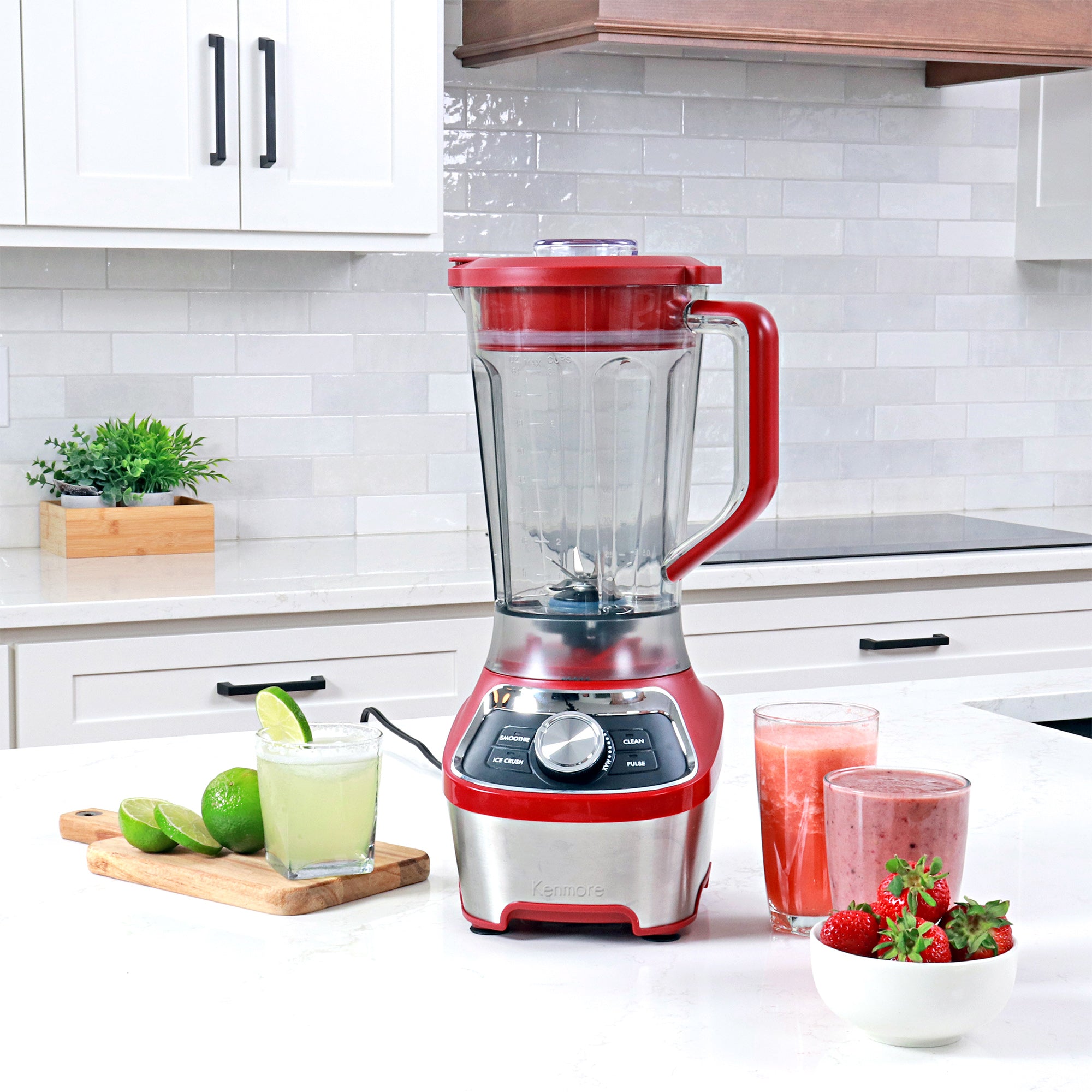 64 oz stand blender on a white countertop with glasses of juice, smoothie, and frozen lime margarita and a bowl of strawberries arranged around it.