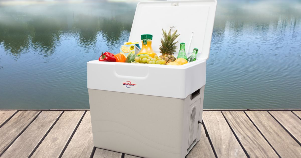 Photo of an open gray and white cooler filled with food and drinks on a wooden dock with a lake in the background