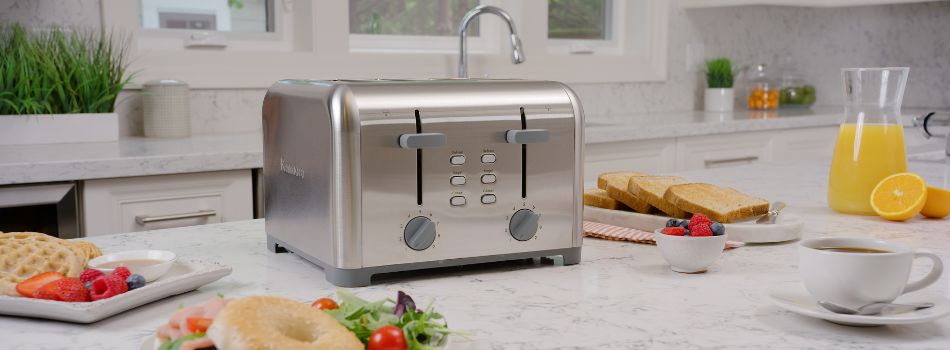 Stainless steel four slice toaster on a white marble counter surrounded by breakfast foods