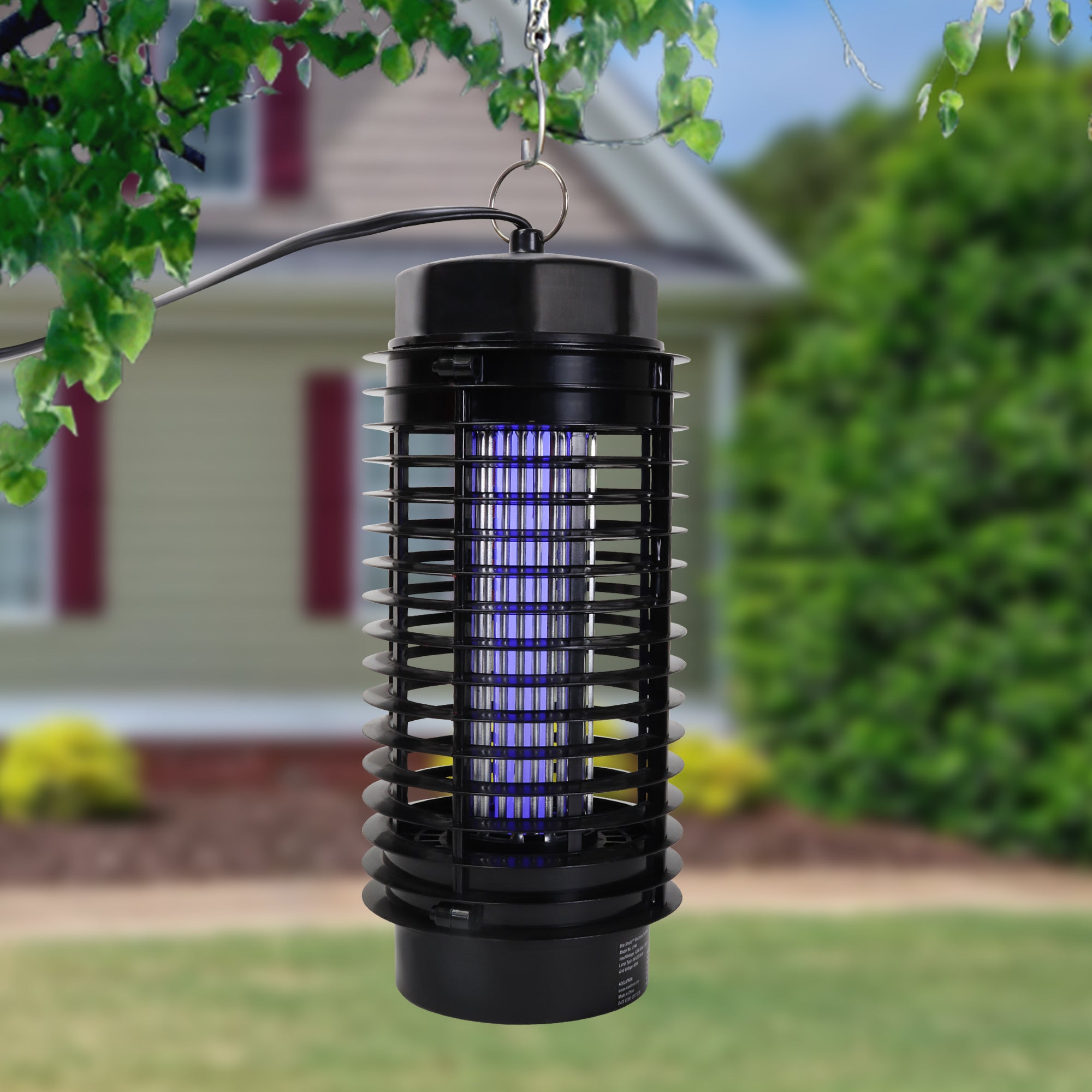 Bite Shield electronic flying insect zapper hanging from a tree branch with a lawn, house, and bushes in the background