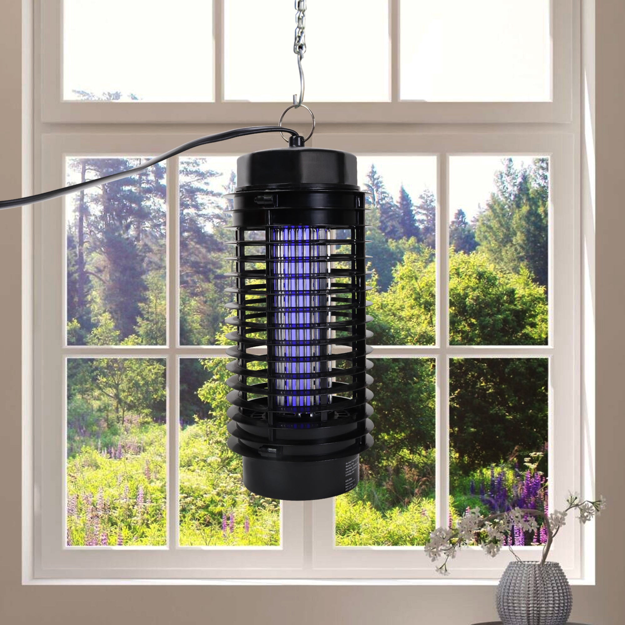 Bite Shield electronic flying insect zapper hanging from a hook in front of a window with a view of bushes and trees outside