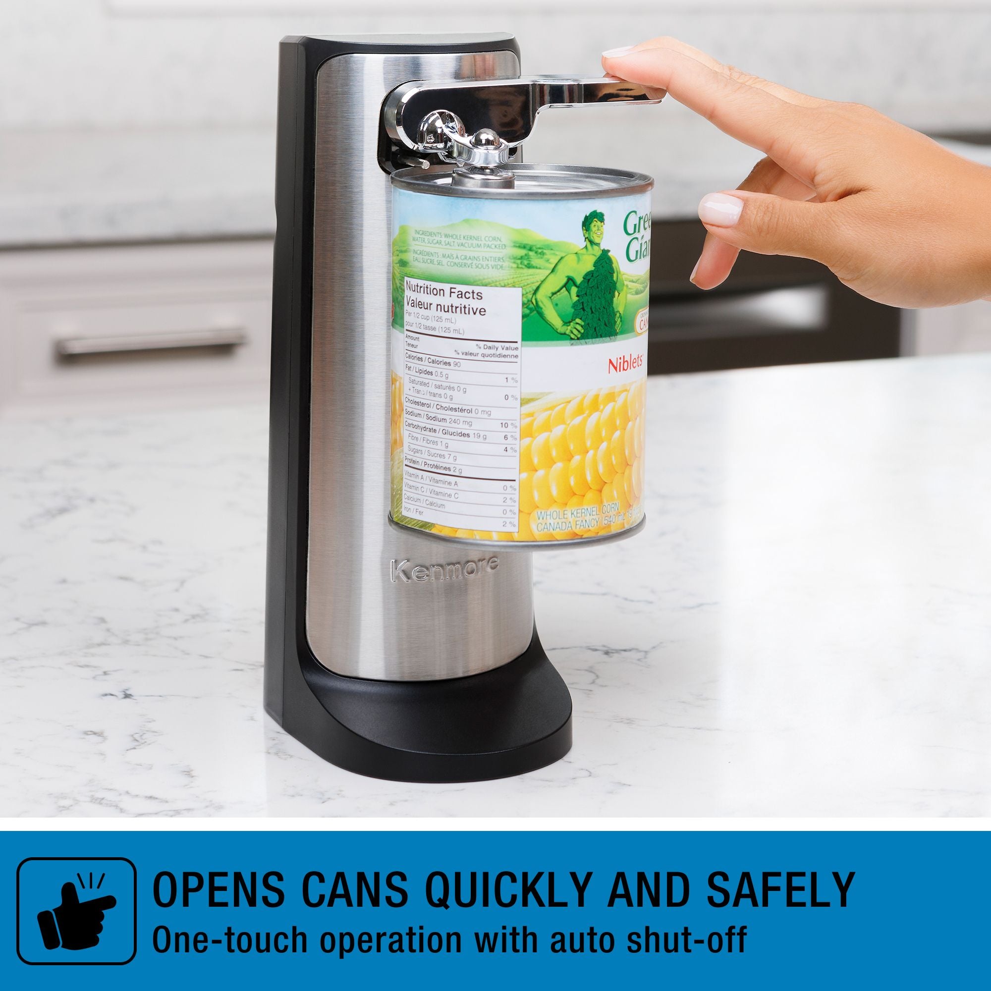 Kenmore automatic electric can opener on a white marble kitchen counter with a can of corn positioned below the cutting lever and a person's fingers touching the lever. Text below reads, "OPENS CANS QUICKLY AND SAFELY: One-touch operation with auto shut-off"