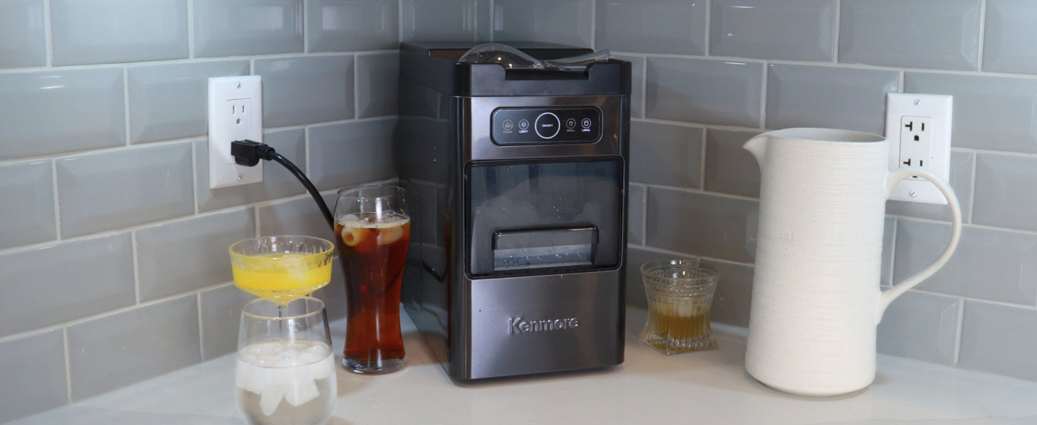 Kenmore front-load ice maker on a white counter surrounded by glasses of iced drinks