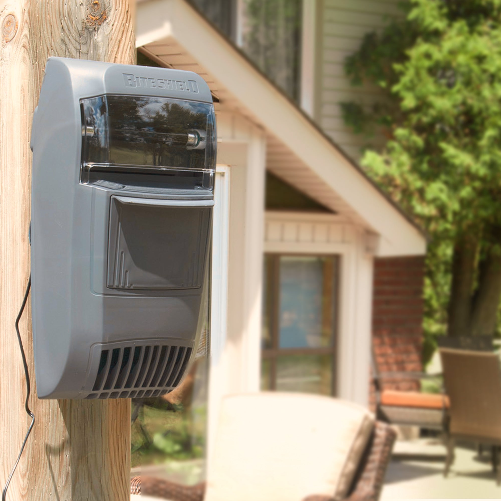 Bite Shield wall mount flying insect trap attached to a wooden post outdoors with the exterior of a house in the background.