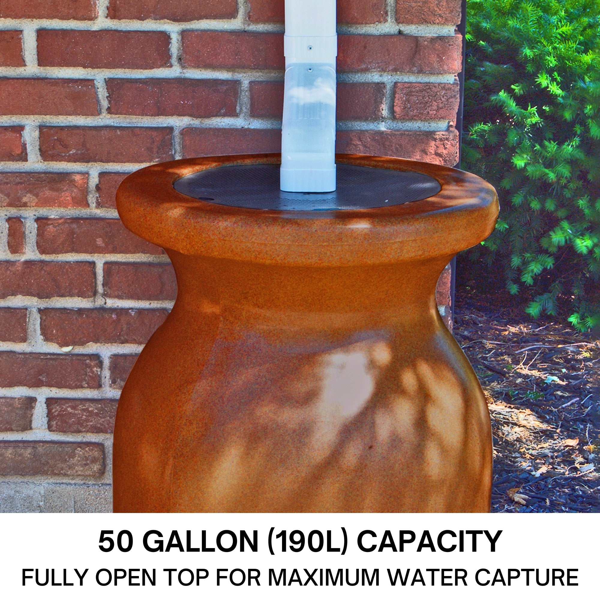 Closeup of the top half of a Koolscapes decorative sandstone-look rainwater urn set up below a white downspout with a red brick wall in the background. Text below reads, "50 gallon (190L) capacity: Fully open top for maximum water capture."