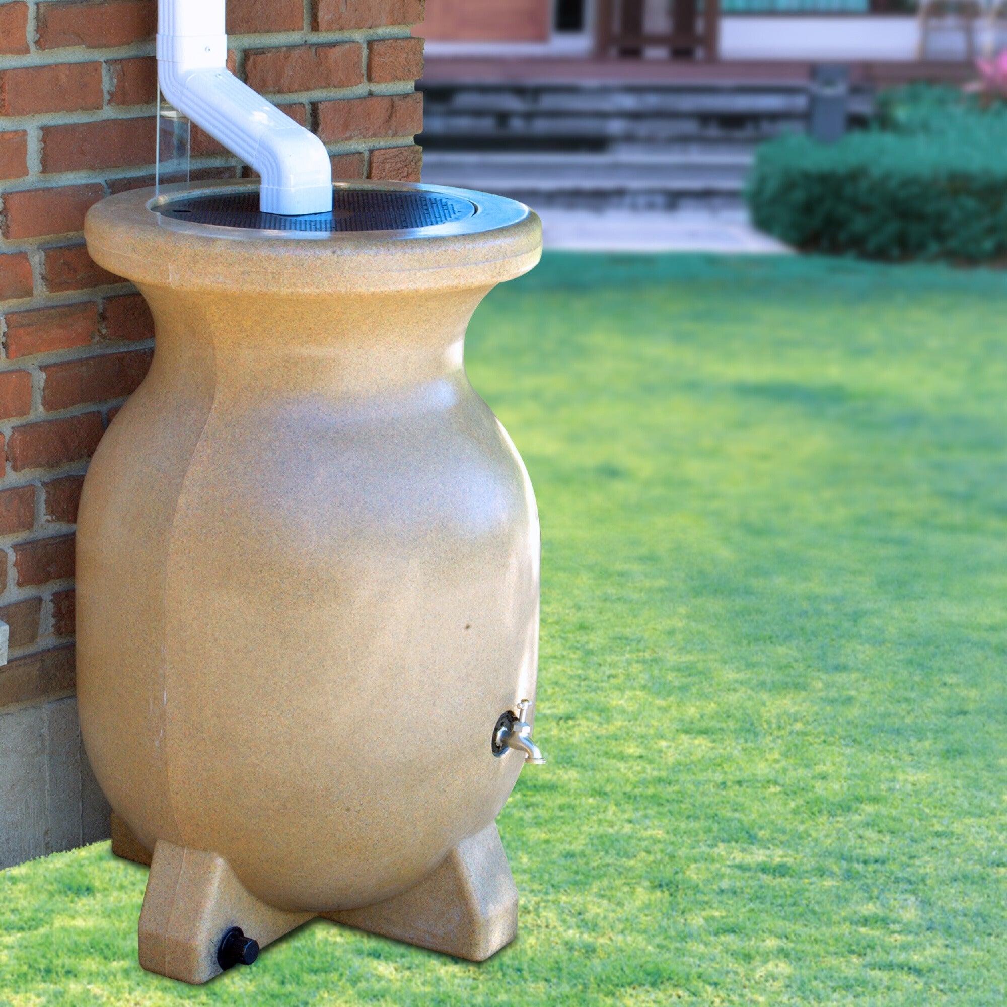 Koolscapes rain barrel set up below a white downspout with a red brick wall and a garden in the background