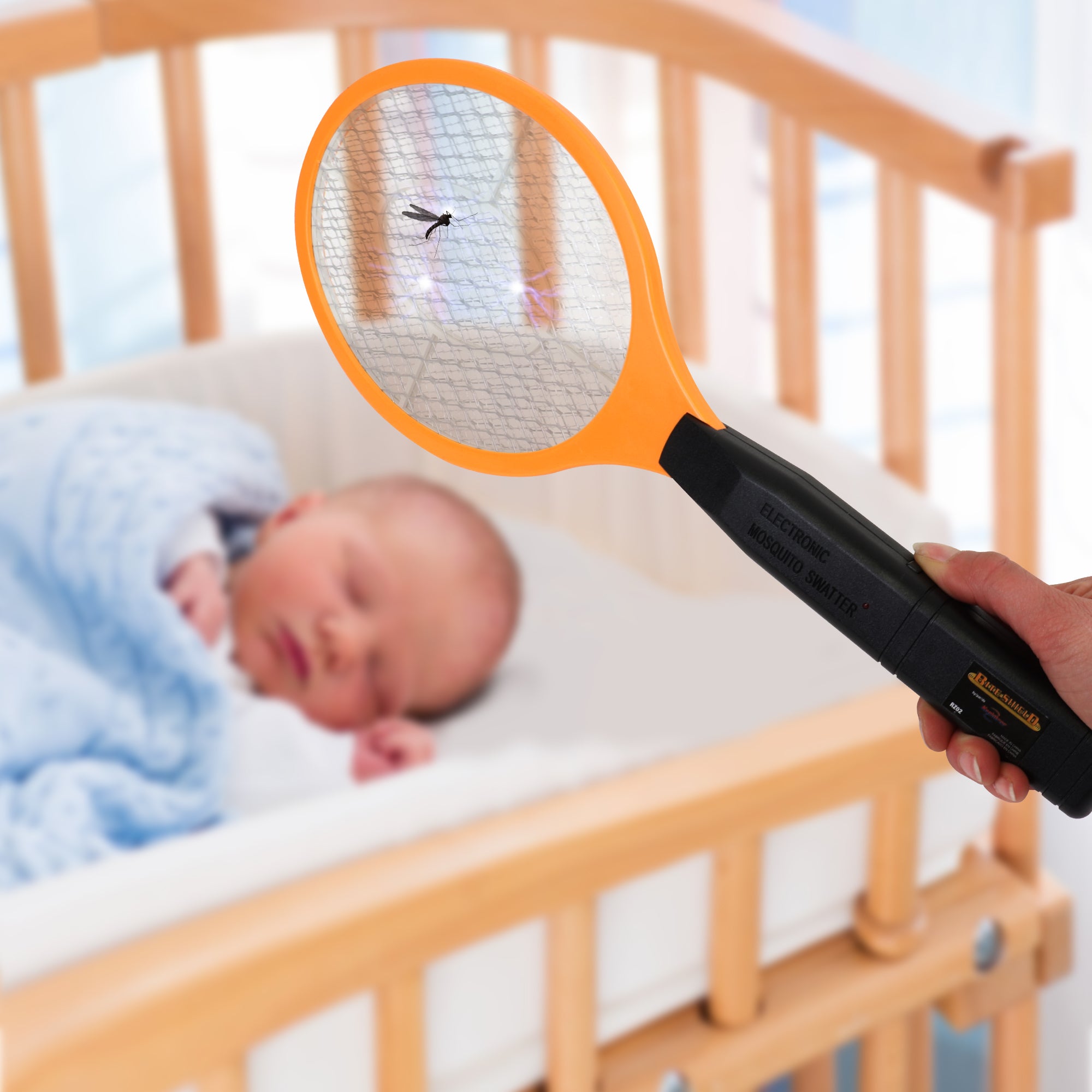 A hand waving Bite Shield racket zapper electronic insect killer over an infant asleep in a crib