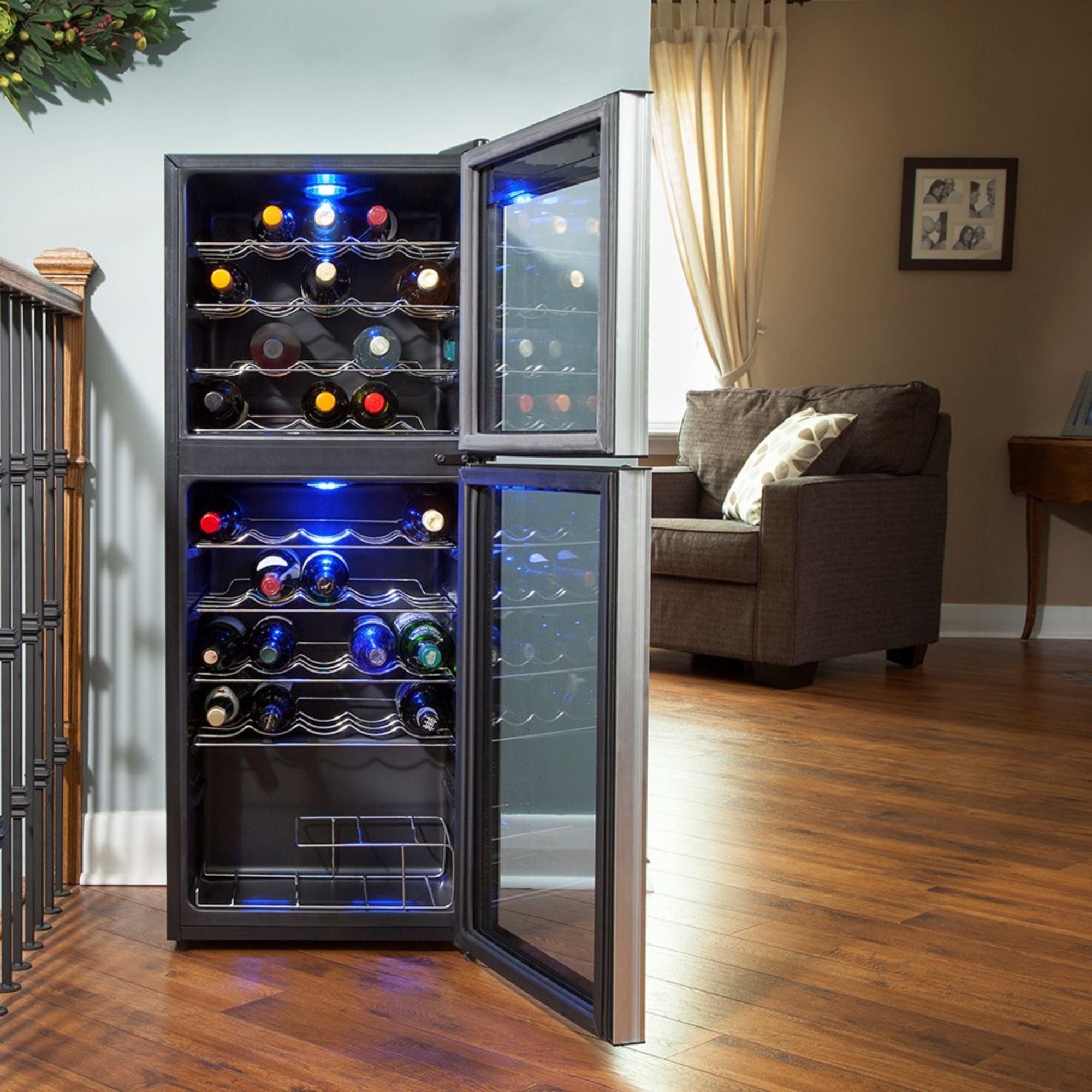 Koolatron 45 bottle dual zone freestanding wine fridge, open and filled with bottles of wine, set up on reddish-brown hardwood floor with a brown sofa in the background